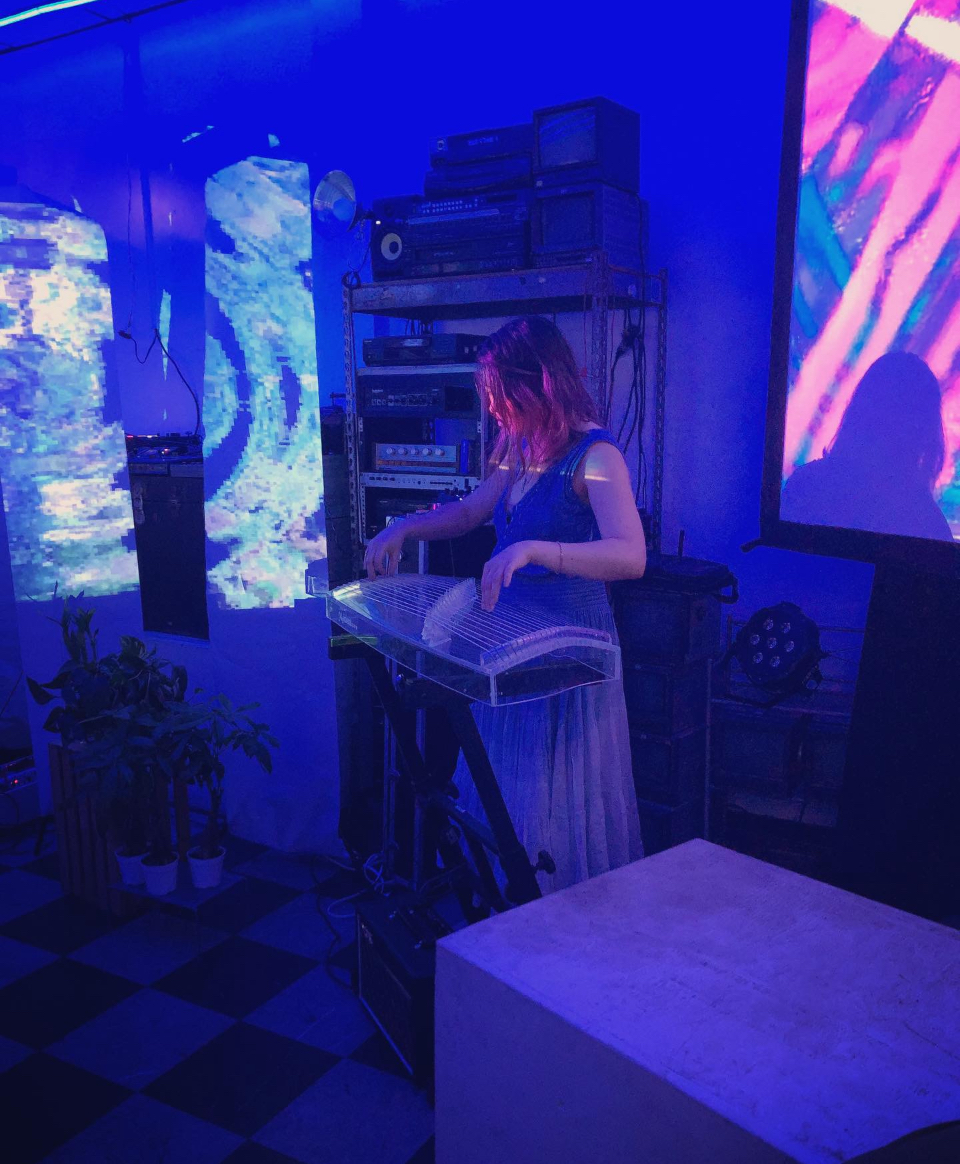 Playing the electronic zither live, surrounded by CRT monitors and VHS decks, projected visuals behind