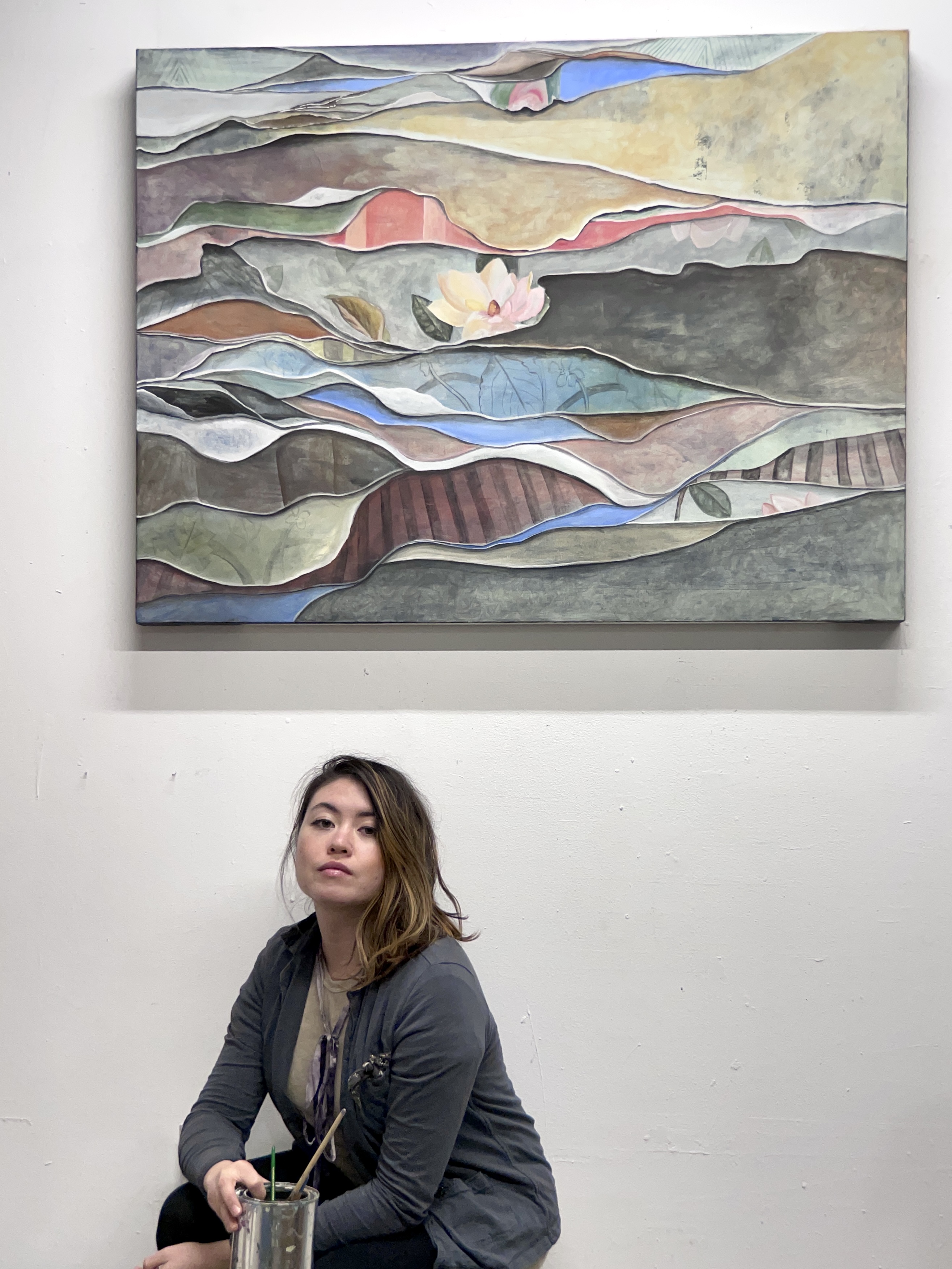 Nadine in the studio beneath a layered landscape painting with a magnolia bloom